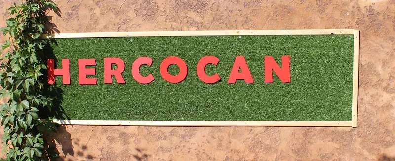 Cartel con letras rojas hercocan sobre panel de césped artificial y marco claro en pared