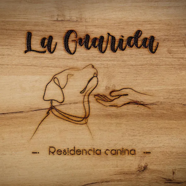 Cartel grabado en madera con el texto la guarida residencia canina y la silueta de un perro olfateando una mano.