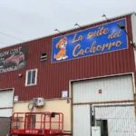 Fachada de nave industrial con un gran cartel azul de la suite del cachorro y dibujo de un cachorro